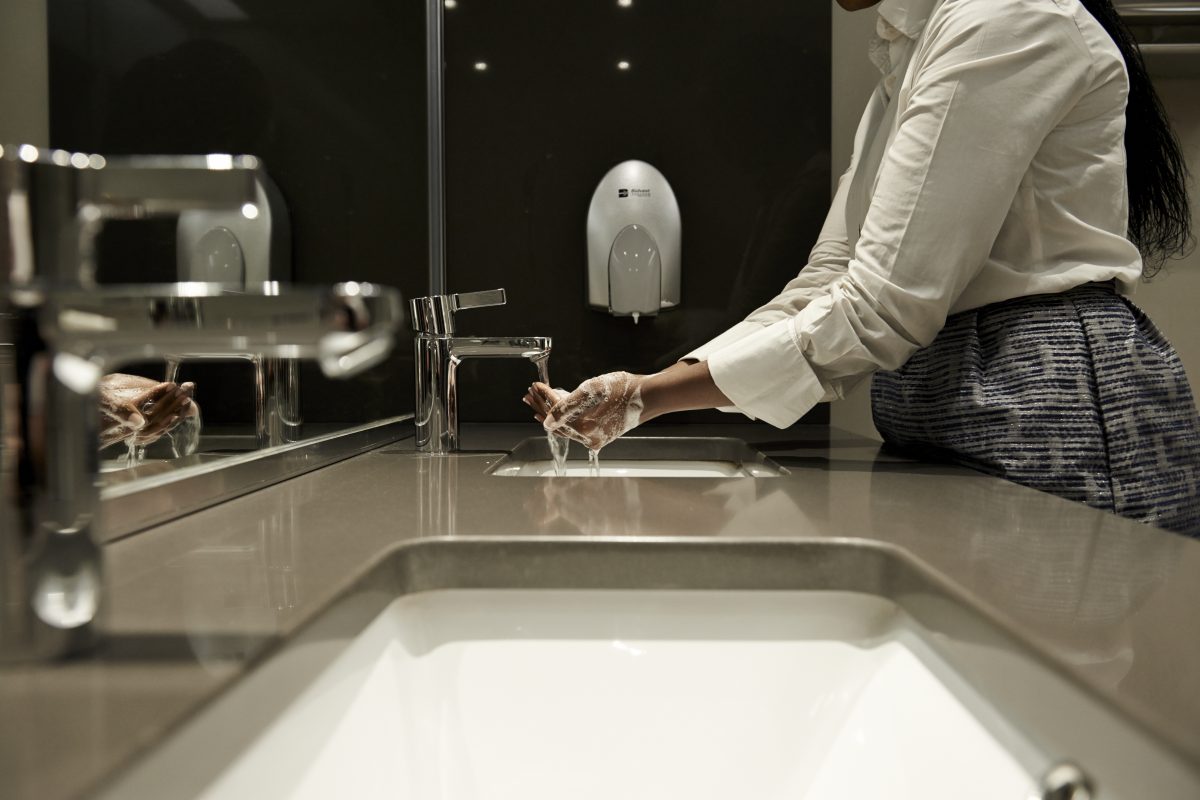 Woman in a public bathroom washing her hands, with a Bidvest Steiner soap dispenser in the back. Rent hygiene equipment today